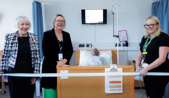 Staff and guests celebrate the official opening of the training hospital ward. One woman is cutting a ribbon.