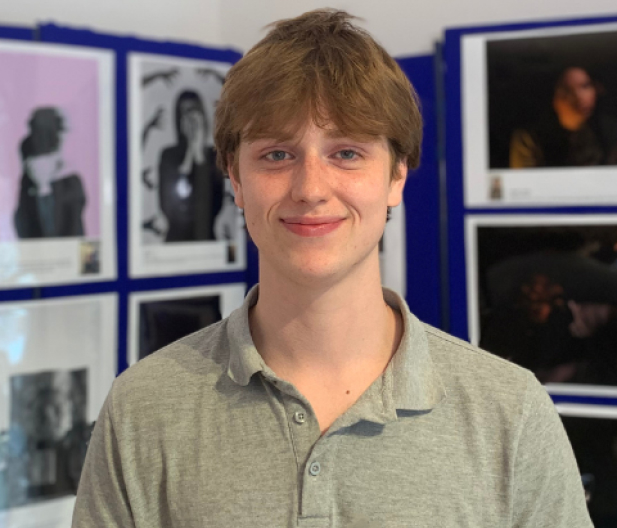 Student in grey t-shirt in front of media and creative arts exhibition displaying student work