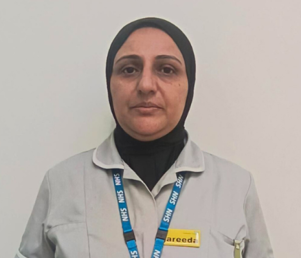 lady with headscarf wearing a grey healthcare uniform with a blue NHS landyard