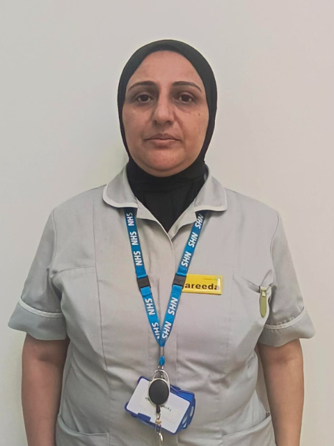 lady with headscarf wearing a grey healthcare uniform with a blue NHS landyard