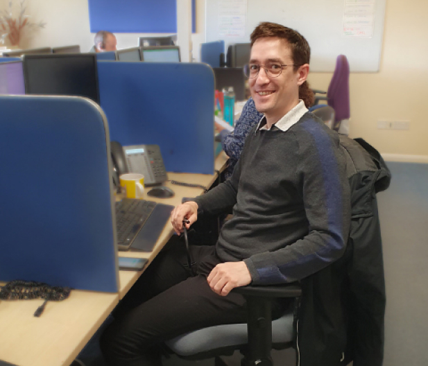 A man smiles while seated at his desk in a professional office setting