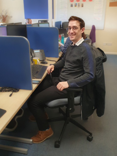 A man smiles while seated at his desk in a professional office setting