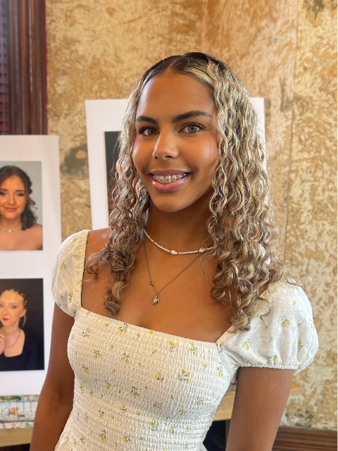 student with braces and curly hair smiling in a dress